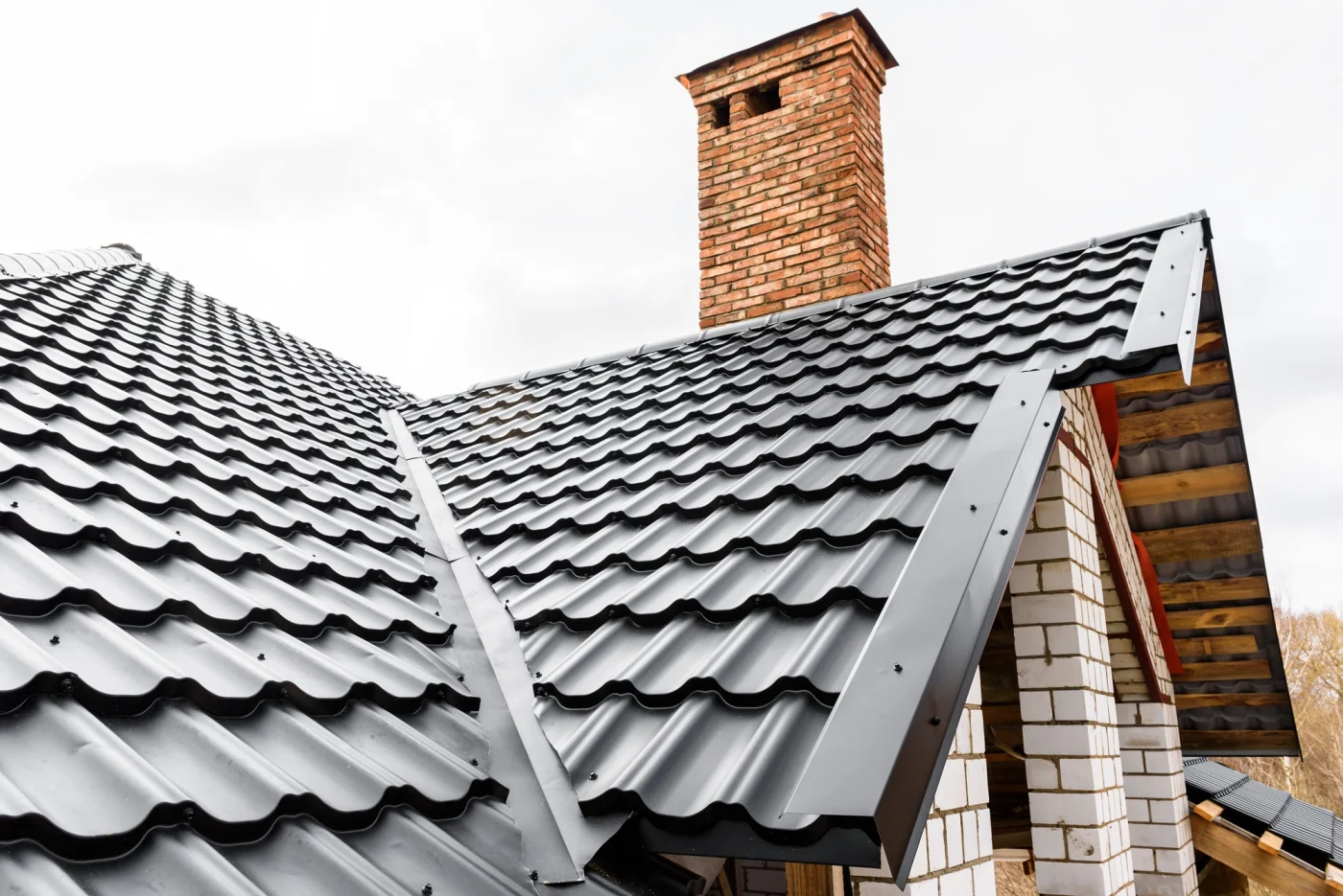 Angled view of slanted roof with black tiles and a brick chimney