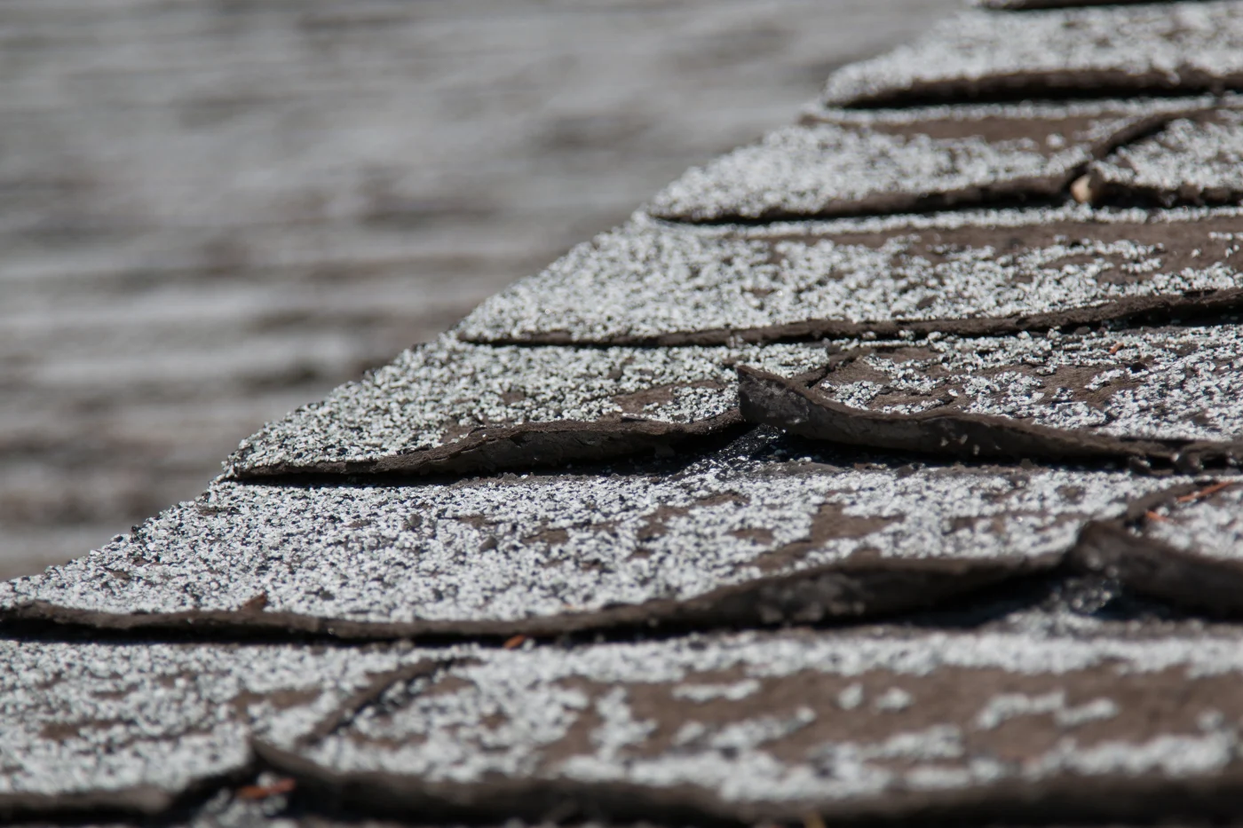 Old Worn Out Asphalt Shingles On The Roof Of A Residential Home. A close-up on an old residential roof, showing some old, curling asphalt shingles that have lost most of their granules.
