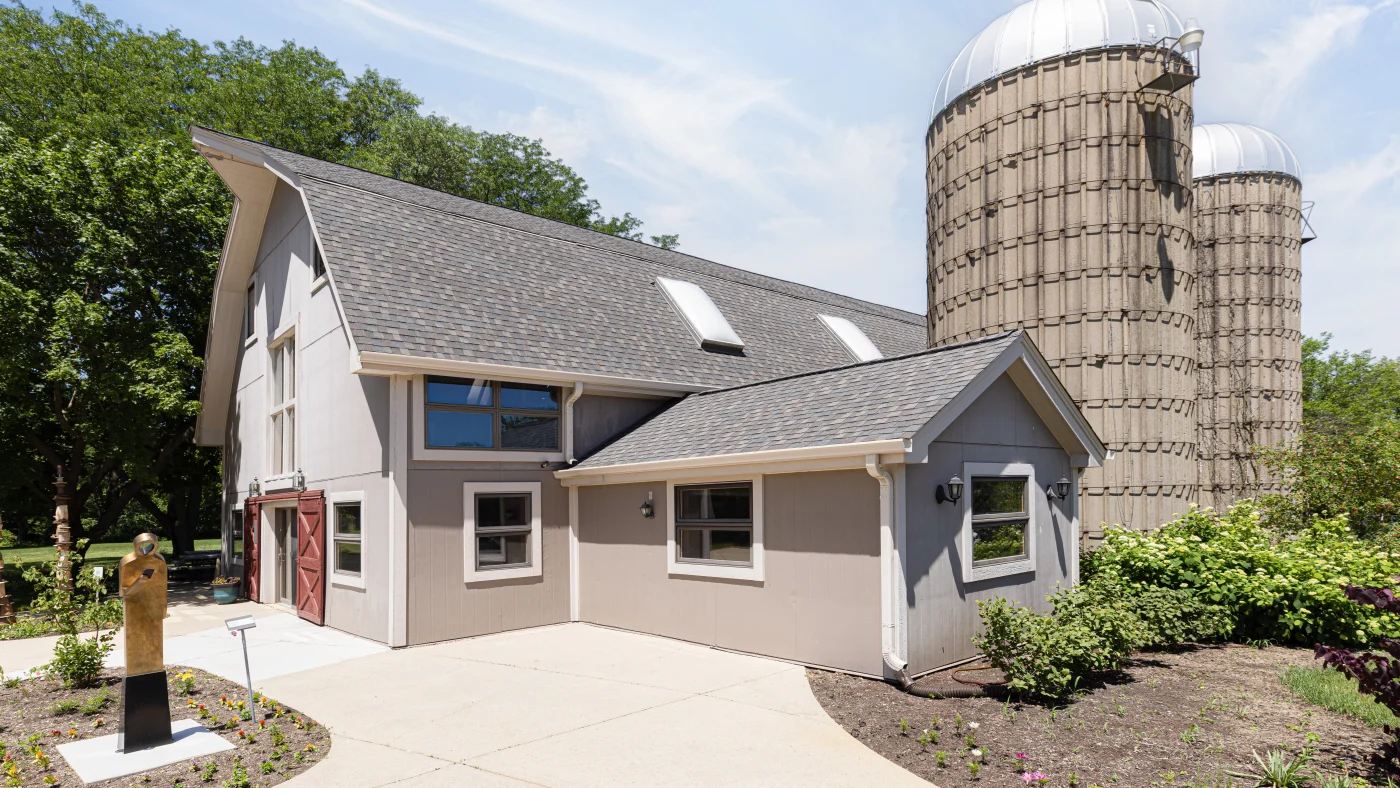 Creative Art Center with gray siding and gray asphalt shingle roof next to two gray color silod