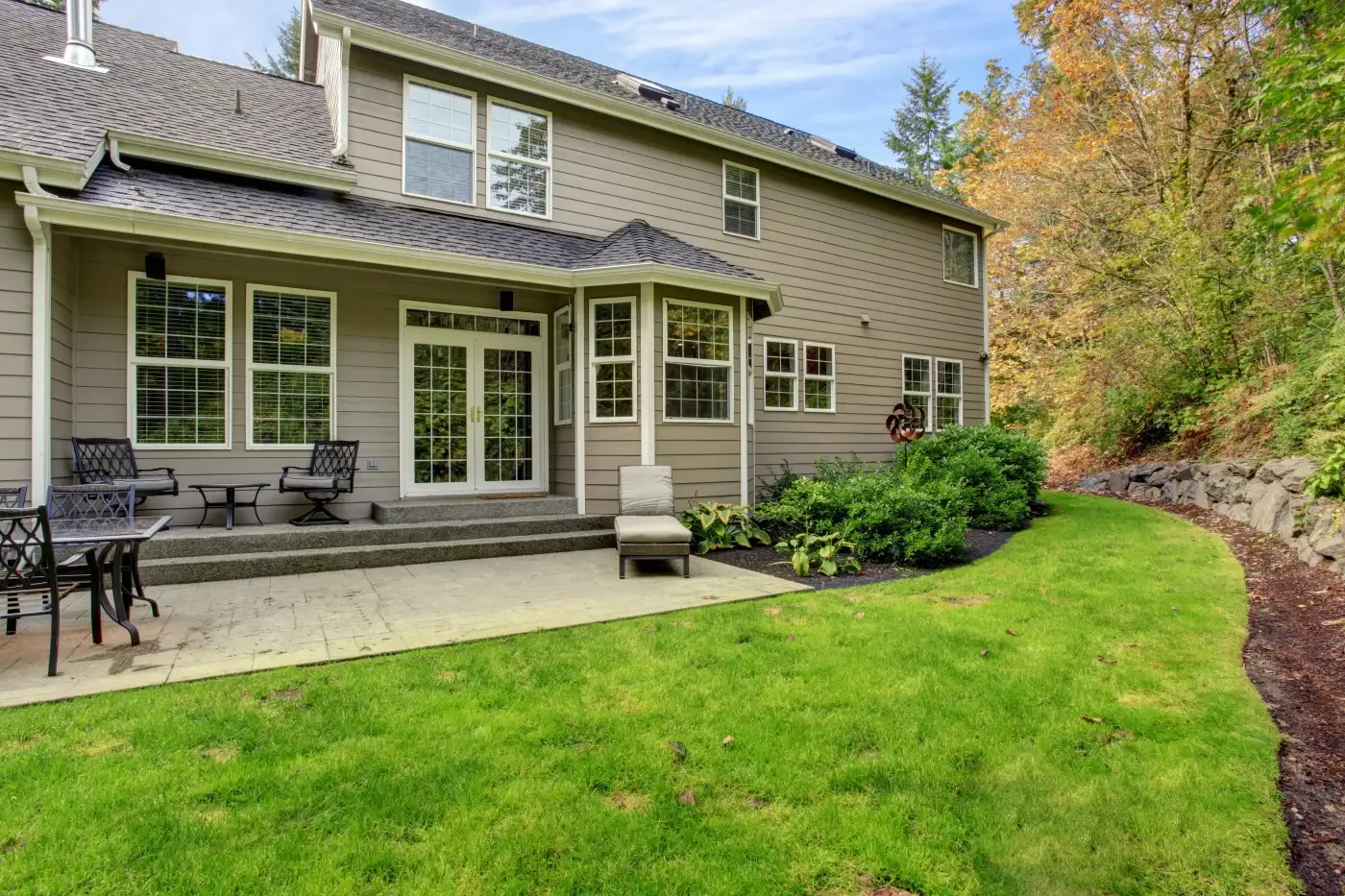 Any Style & Configuration Patio Door Replacement In The Chicagoland Area The back of a two-story home with light brown horizontal panel siding, light gutters and fascia, as well as white windows with blinds and a set of French patio doors with bronze hardware.
