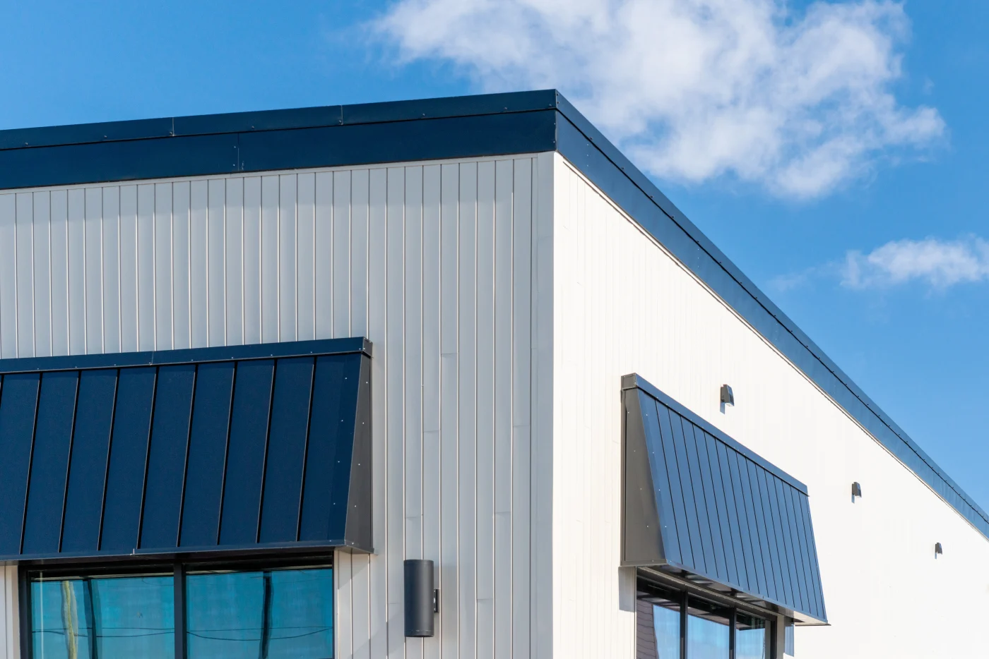 Close-up view of modern commercial building exterior featuring vertical metal siding panels and dark metal awnings. Clean lines, durable materials, and sharp detailing showcase high-performance siding solutions used in new commercial construction projects for long-term protection and visual appeal.