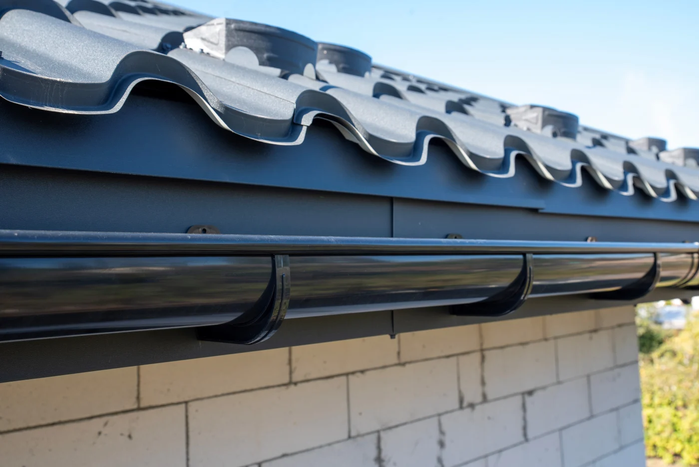A close-up on a new dark gutter system above a white brick wall shows a clean, professional installation.