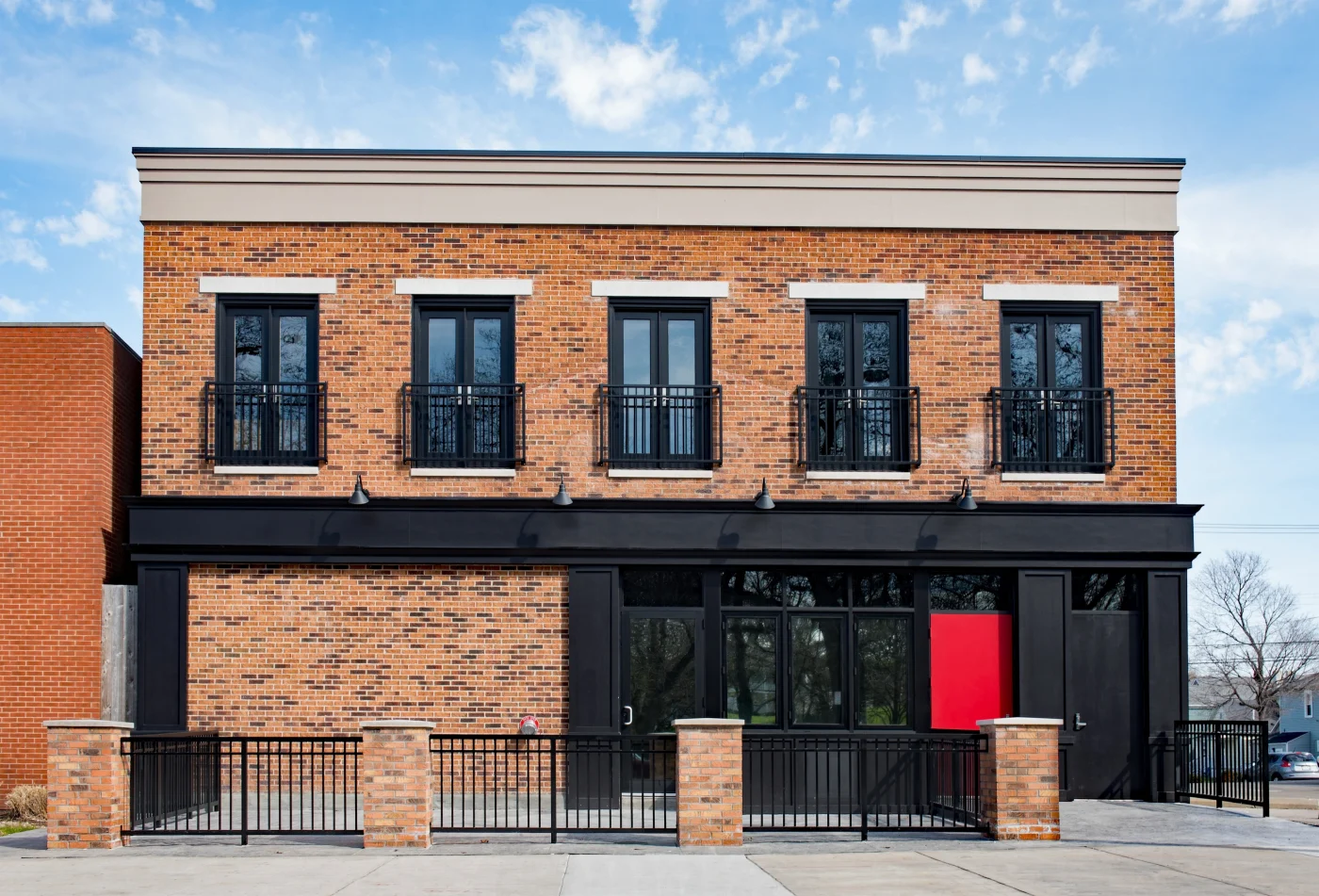 A beautiful smaller commercial brick building with new dark black accents for the doors and railings upstairs, all the pillars, and the entrance area.