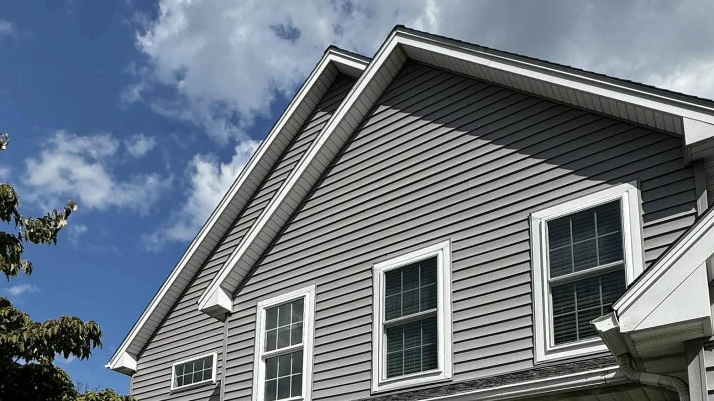 On the top side of a home on a slightly cloudy, blue day, light gray horizontal panel vinyl siding from CertainTeed complements the white windows, soffit, and fascia.