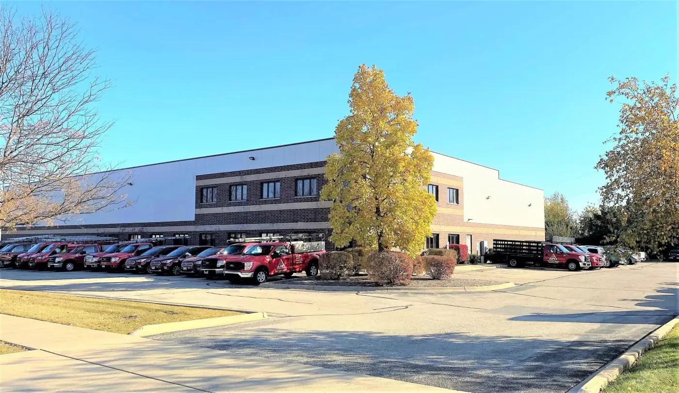 Apex Exteriors – Exterior Remodeling Careers In The Chicagoland Area A wide shot of the large Apex Exteriors company building in South Elgin, Illinois, with lots of different branded vans, cars, trucks, and heavy trucks lined up along both sides of the building.