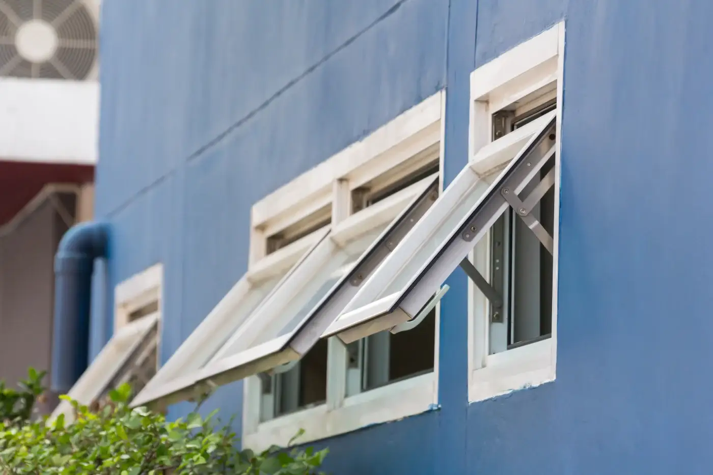 A set of three open white awning windows in the side of a wall with a light blue color.