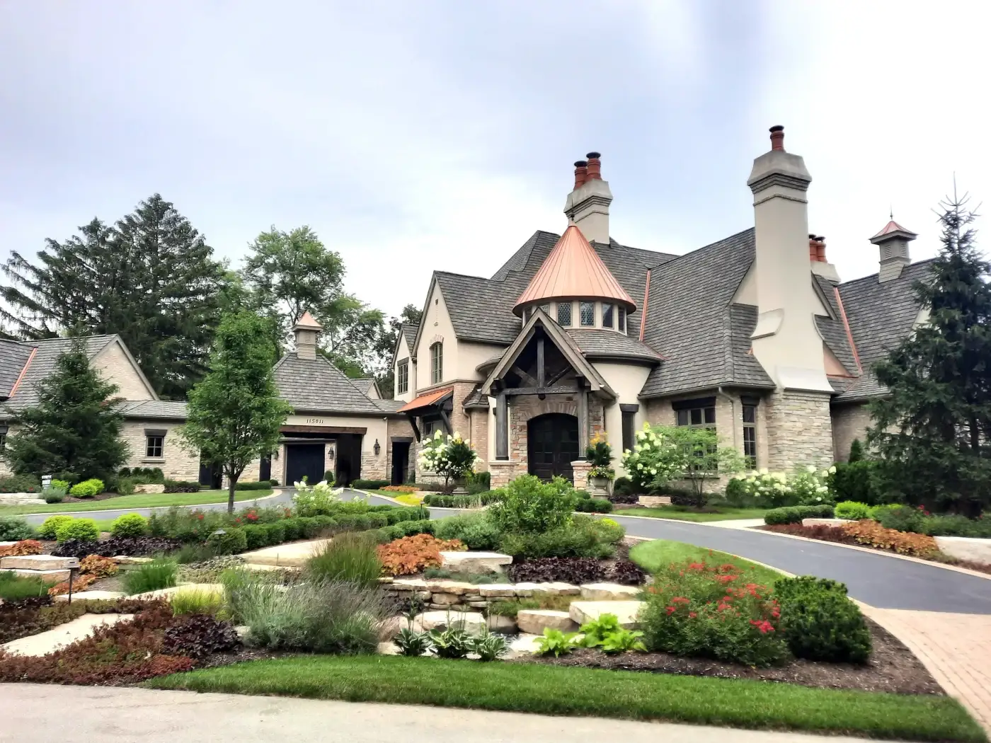 A huge, custom, luxury home with multiple tall chimneys, a complex framework of roofing and architecture, many different custom windows, and professional landscaping in the Chicagoland area.