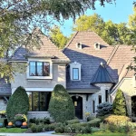 A luxury home in St. Charles, IL, featuring a newly installed DaVinci composite shake roof. The elegant exterior features a blend of light-colored brick and stucco, complemented by architectural details such as arched windows, dormers, and a turret-style roof peak. The synthetic shake shingles blend beautifully with the home’s upscale aesthetic, providing the look of natural cedar with modern durability. Lush landscaping and mature trees frame the property.