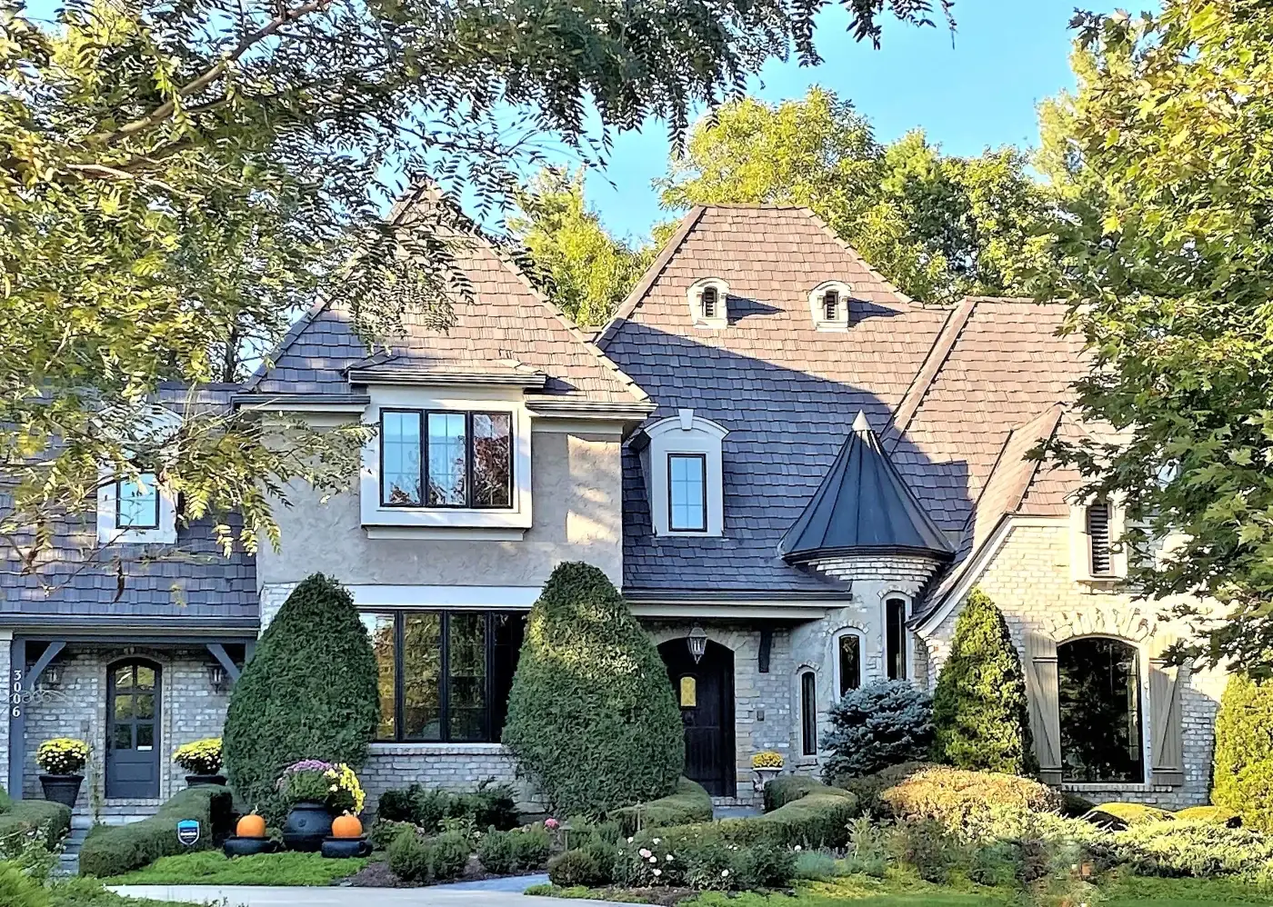 Chicagoland Cedar Shake Roofing Swap With Composite Cedar Shake Roofing A luxury home in St. Charles, IL, featuring a newly installed DaVinci composite shake roof. The elegant exterior features a blend of light-colored brick and stucco, complemented by architectural details such as arched windows, dormers, and a turret-style roof peak. The synthetic shake shingles blend beautifully with the home’s upscale aesthetic, providing the look of natural cedar with modern durability. Lush landscaping and mature trees frame the property.