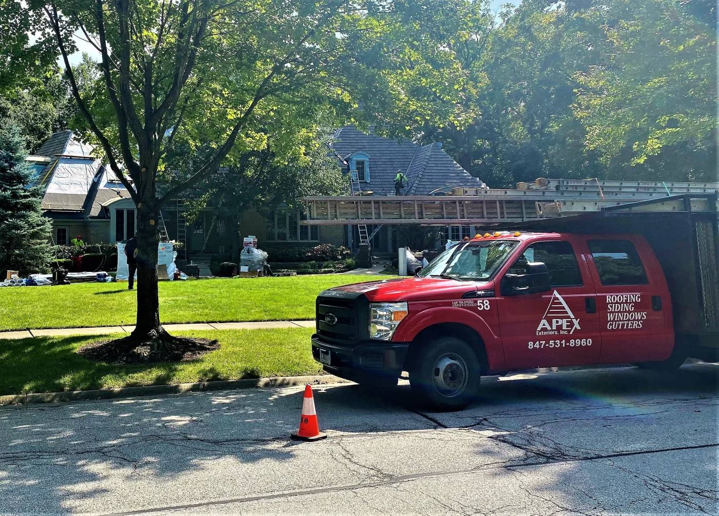 Apex Exteriors Chicagoland Exterior Projects Process – Step 6 – Construction An Apex Exteriors work truck is parked in front of a home under active construction, with roofers visible on the structure. This image shows the professional execution and high-caliber workmanship that define the final project stage with Apex Exteriors.
