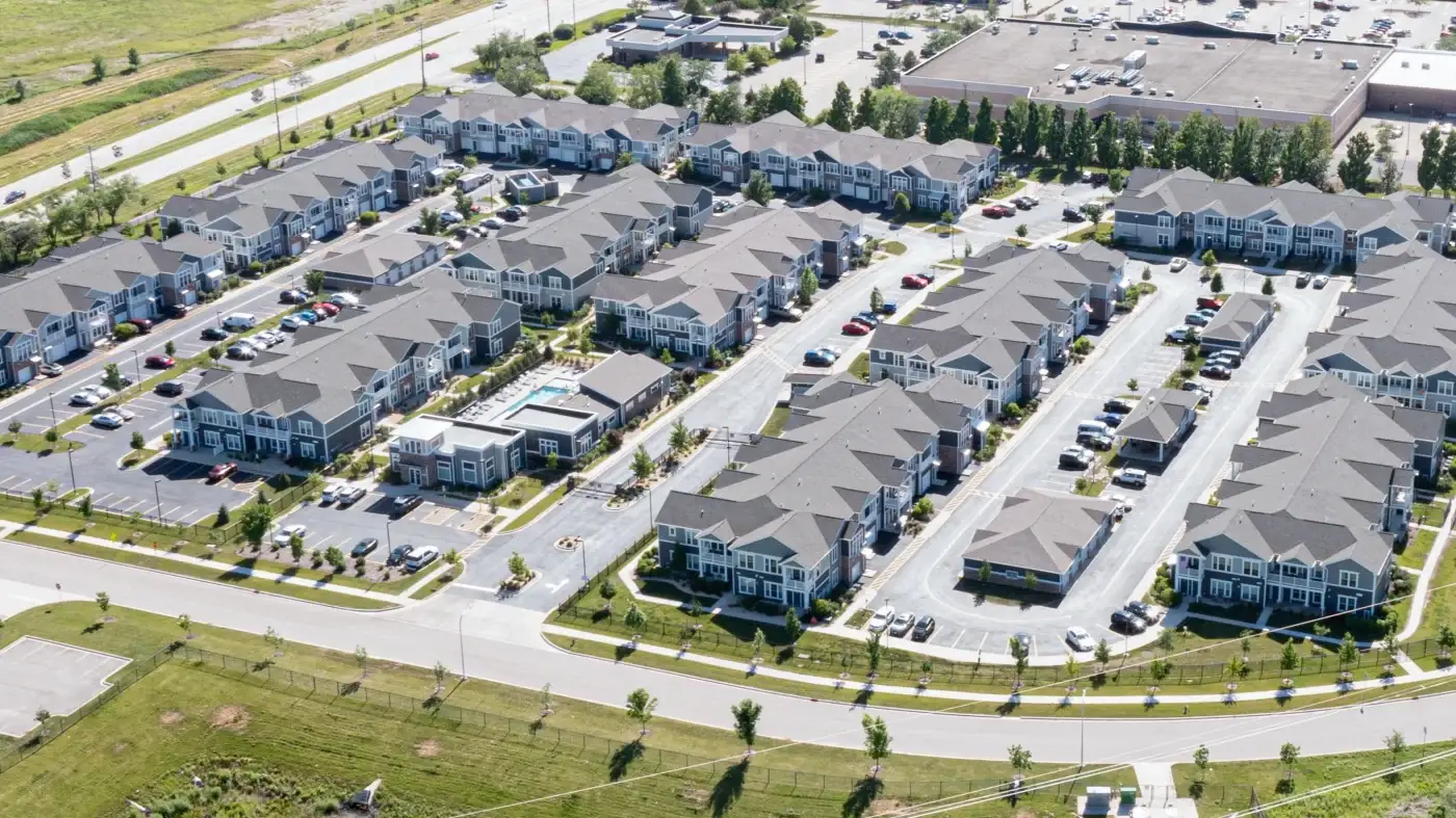 Consistent High-Caliber Workmanship On Large Multi-Family Projects Aerial view of a large, completed multi-family apartment complex in the Chicagoland area. The complex features rows of neatly arranged two-story buildings with gray siding and matching shingle roofing. Streets, parking areas, and landscaped green spaces are visible throughout the property, demonstrating a well-organized, high-quality residential development.