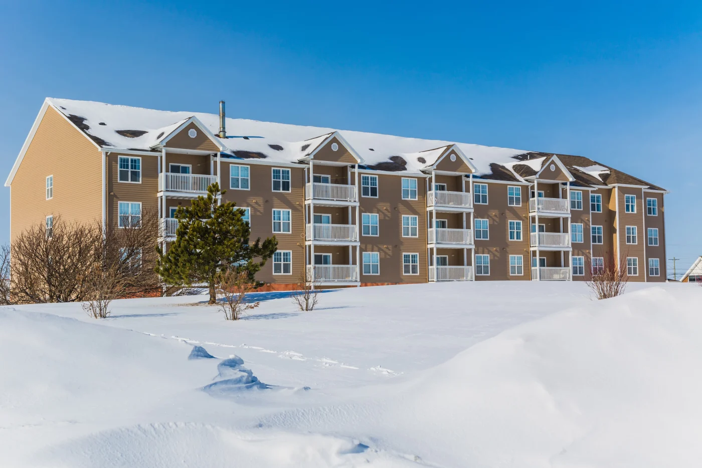 Three-story multi-family building with snow-covered roof and surrounding landscape, illustrating the critical need for gutter systems designed to withstand freeze-thaw cycles and heavy snow loads in Chicagoland.