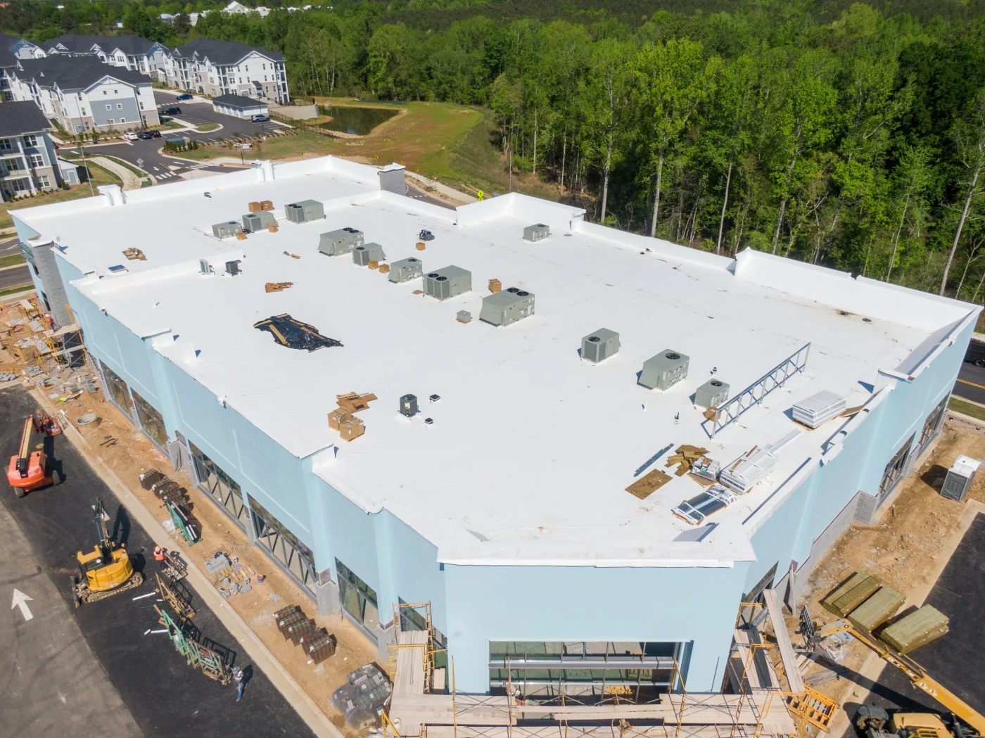 Aerial view of a large commercial building under construction with a completed white flat roof and active jobsite below—illustrating a professionally installed, warranty-eligible roofing system by a fully certified and insured contractor.