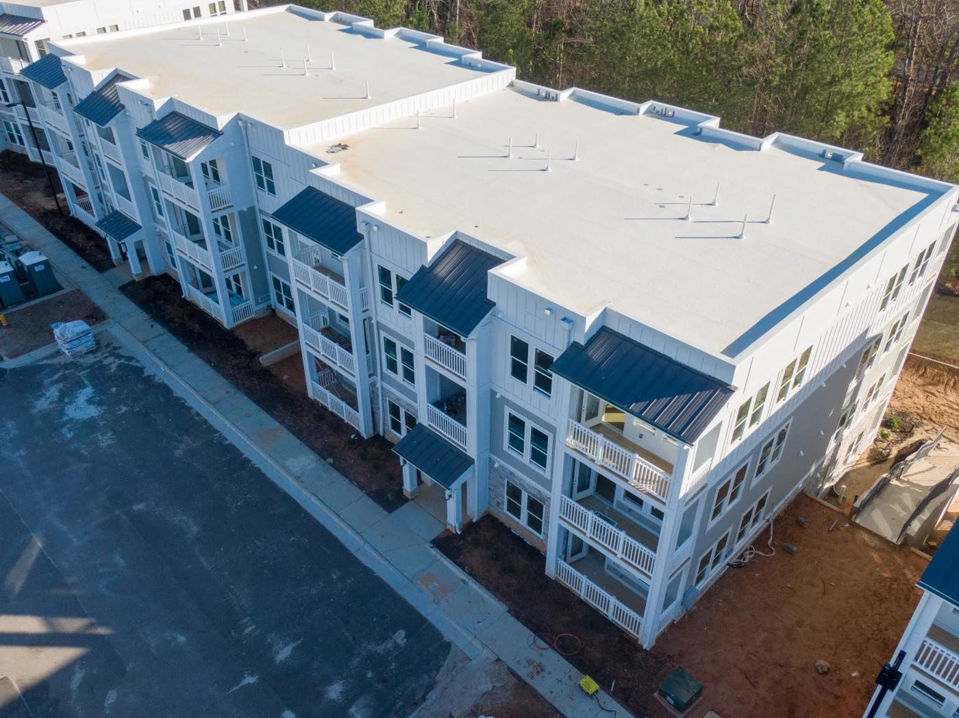Aerial view of a newly constructed multi-family building with a clean white flat roofing system and architectural metal accents—demonstrating a tailored roofing solution designed for durability, efficiency, and aesthetic appeal in large-scale residential construction.