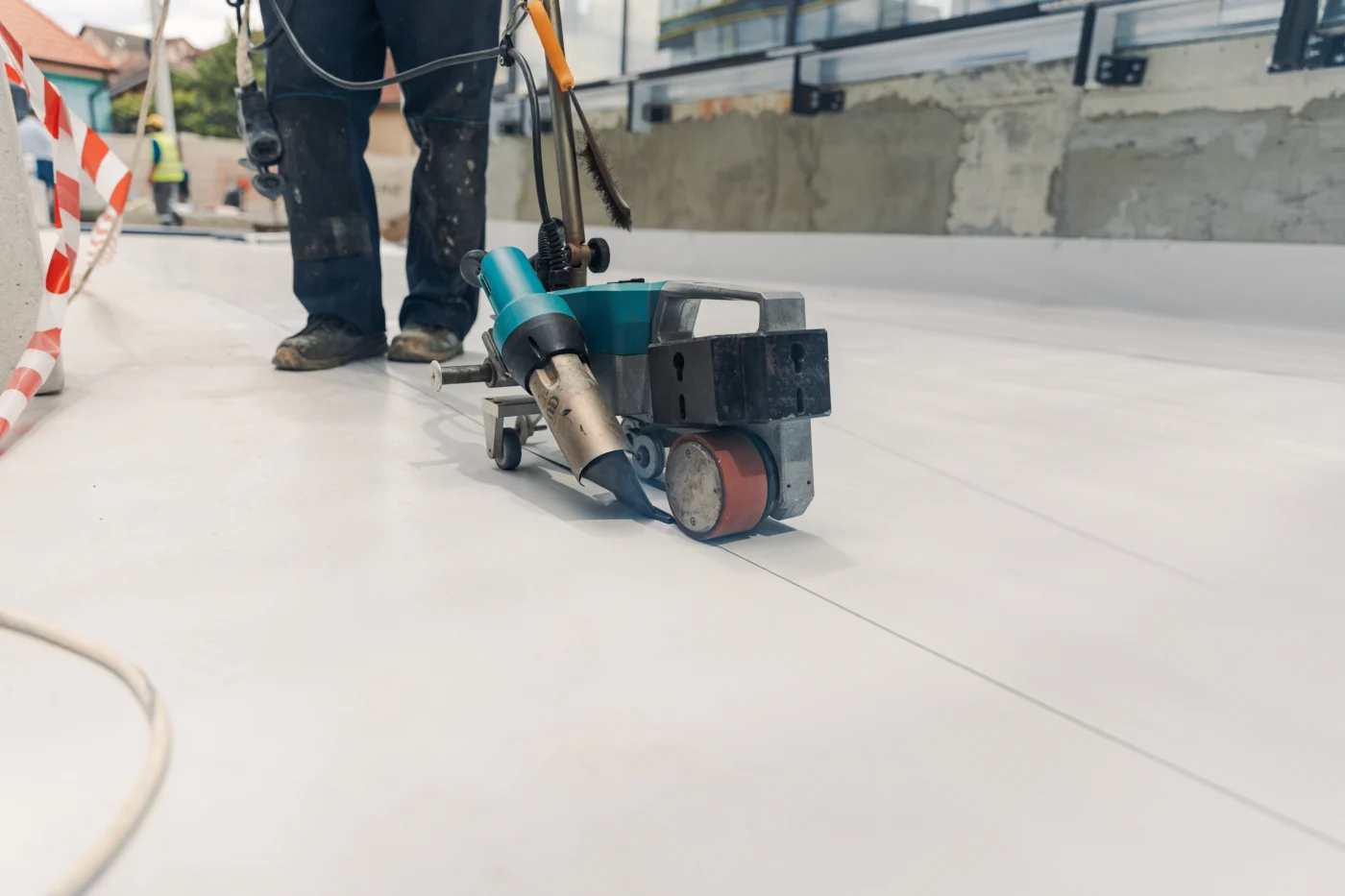 A working is using a special machine to weld or install a PVC commercial roofing system on a building’s roof.