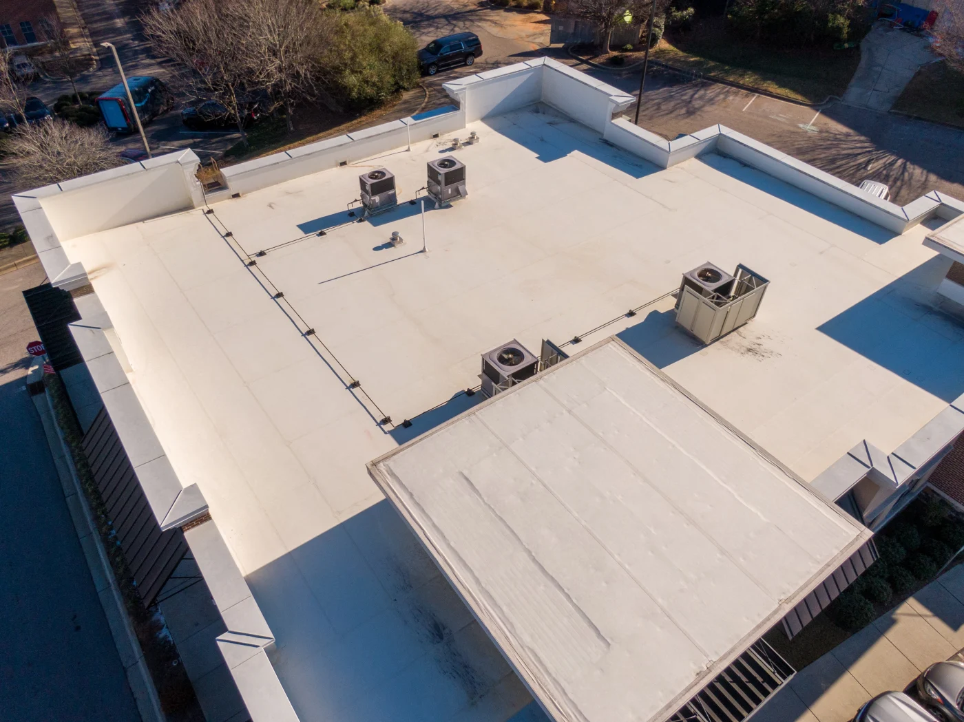 Looking down from the sky on a flat commercial building’s roof with a newly-installed, white TPO roofing system, vents, etc. Around the building is what looks like a residential area.