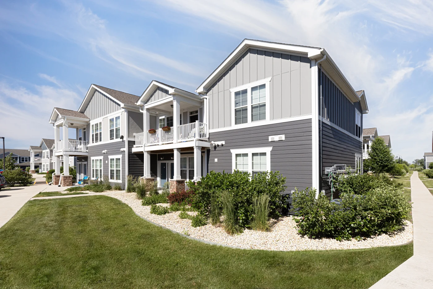 A section of apartments in the Chicagoland area that had an exterior makeover done by Apex Exteriors, with white trim, fascia, windows, pillars, and railing, as well as lightly-toned horizontal panel siding on the bottom and vertical panel siding on the top section of the buildings, as well as new premium shingle roofing.
