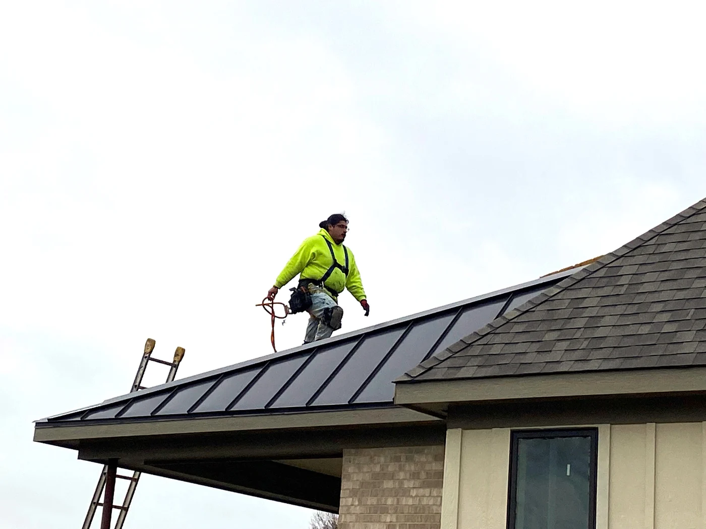 An Apex Exteriors roofer walks on a newly installed metal roofing system wearing protective gear and a harness.