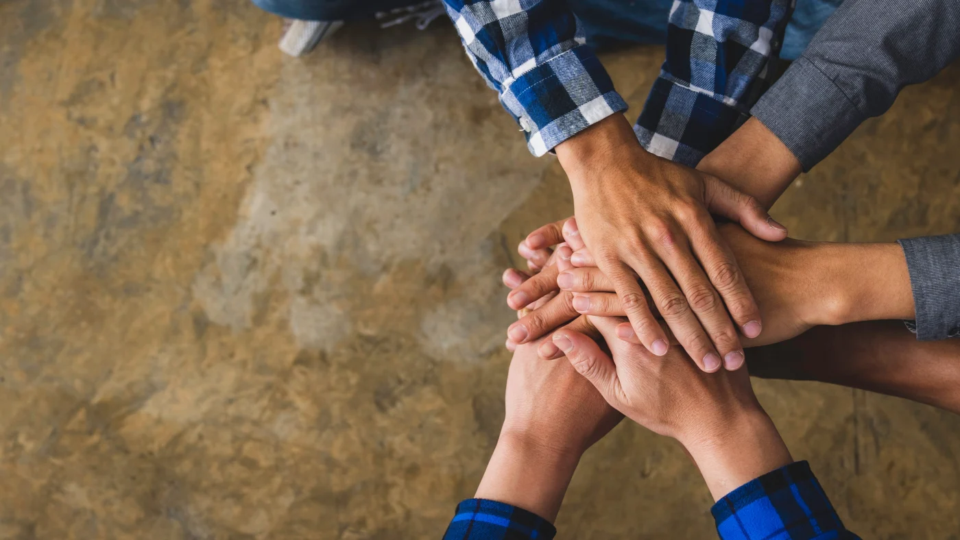 Four people join their hands together in a spot in the air, symbolizing collaboration and commitment.