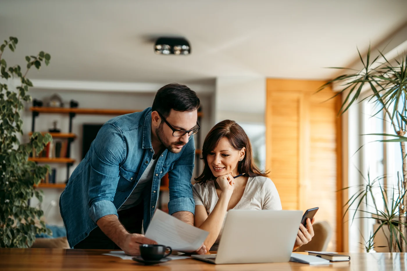 Residential & Commercial Exterior Remodeling Without Nonsense Pricing Games A couple smiling, looking at a laptop and an exterior remodeling estimate together at their open-concept kitchen counter.