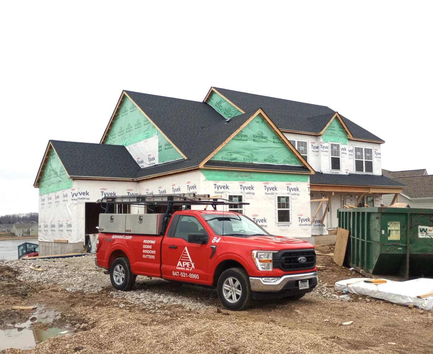 Apex Exteriors Partners With Elite Product Material Brands Exterior Remodeling Chicagoland A new residential construction worksite with an Apex Exteriors work truck in what will become a driveway area, with the main structure of the large luxury home built, with Tyvek and Kingspan housewrap showing, and brand new dark shingle roofing.