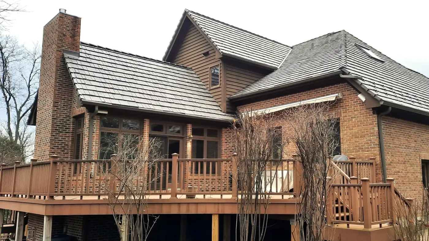 Any Type Of Patio Door Material – Patio Door Replacement In The Chicagoland Area A large brick home in the Chicagoland region with a shake roof and sections of panel siding, a large back patio wood deck with stairs, as well as a dark brown patio door with lots of similarly colored windows around the area.