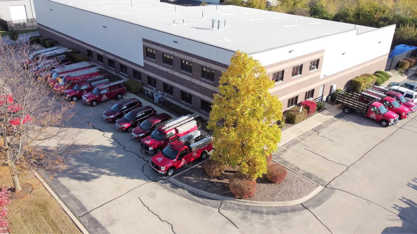 Apex Exteriors Provides Professional Exterior Remodeling Insights & Recommendations A drone shot of the large two-story Apex Exteriors headquarters or company building in South Elgin, Illinois, with red and black company cars, work trucks, and vans lining the outside on a sunny morning.