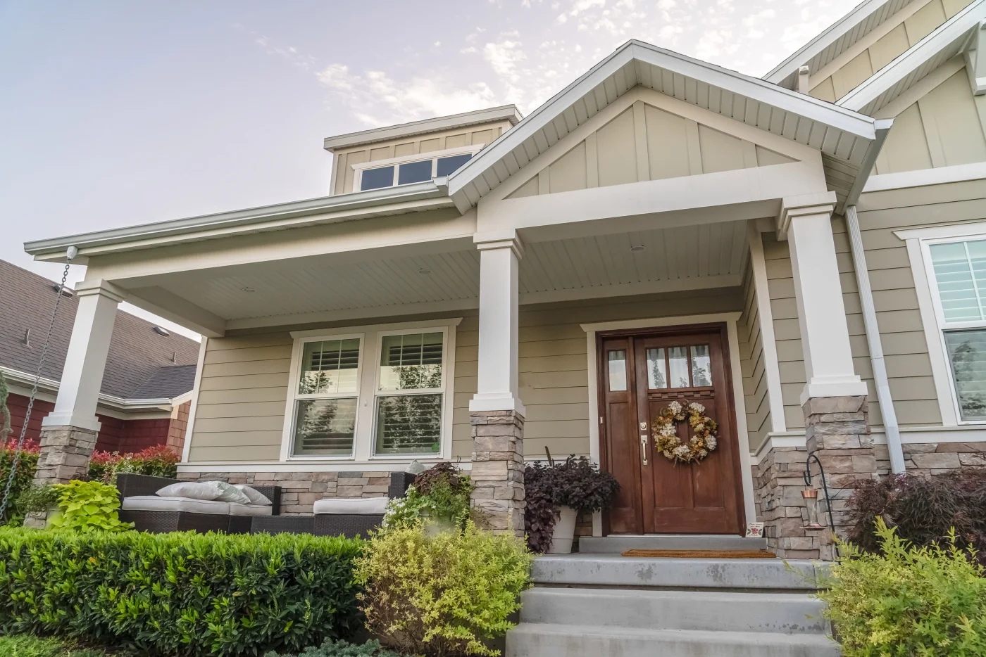 Angled view of home with beige siding,  white framed replacement windows, and a beautiful wood-stained door with a wreath