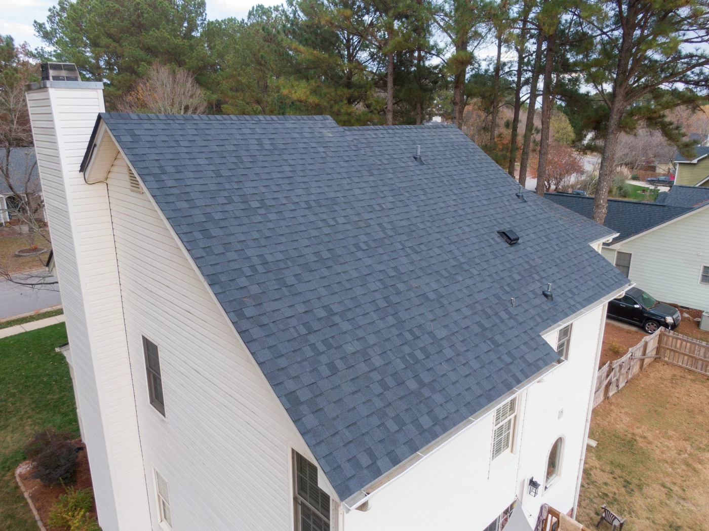Chicagoland Residential Roof Replacement Services A close-up drone shot of a residential home with white panel siding and new dark gray shingle roofing, with trees in the background and other similar homes with similar roofing systems.