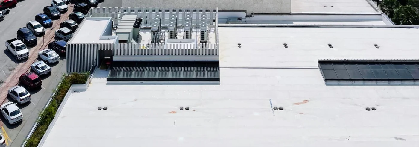 Image of a large, white commercial roof on a building next to a parking lot