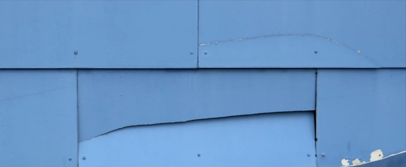 Close-up image of damaged, blue siding on a wall