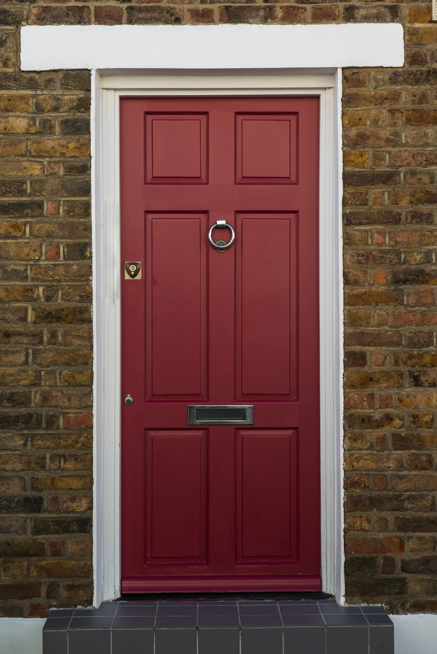 A striking red entry door with an elegant knocker set into a brick wall.