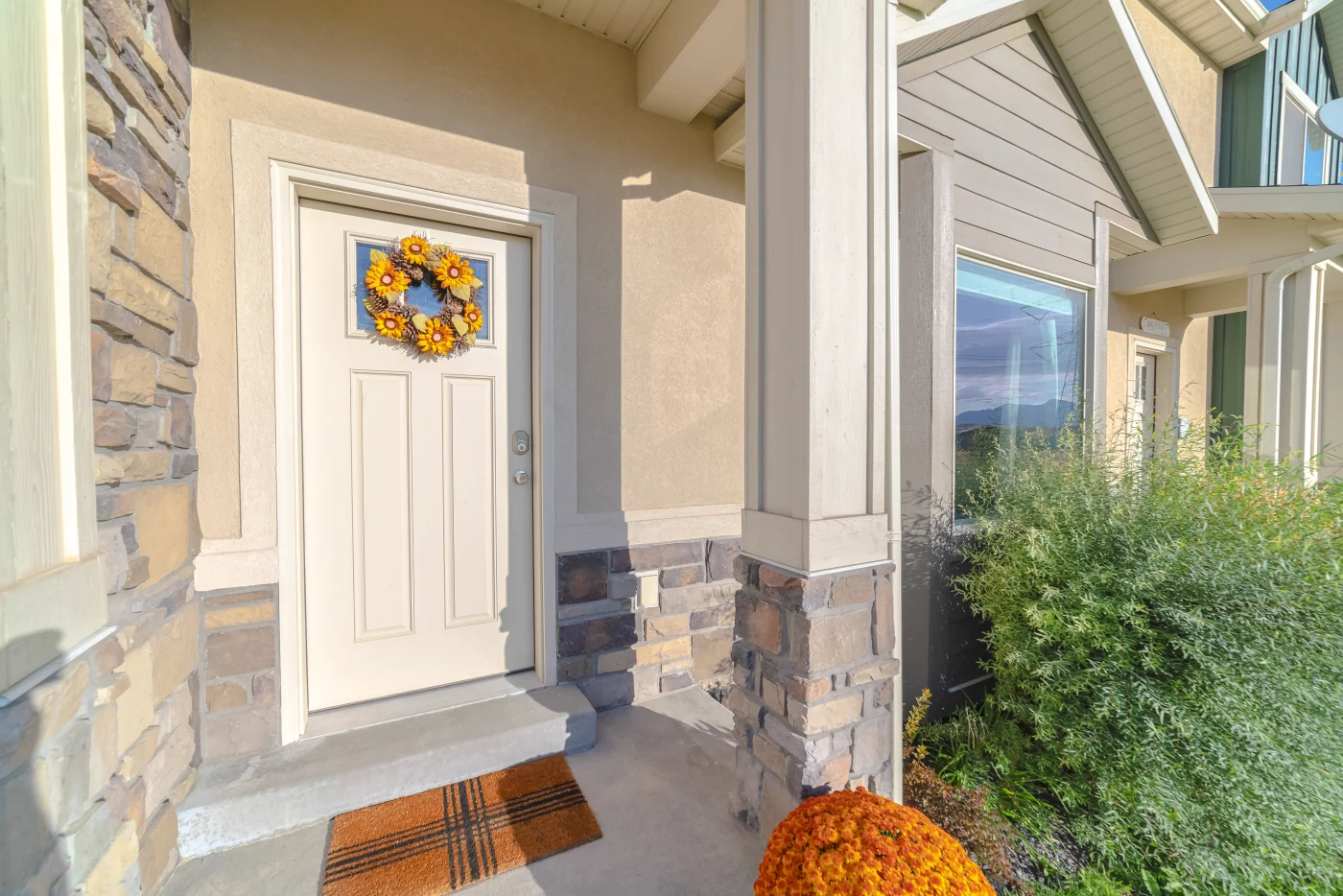 Image of a white entry door with an orange wreath on a home with stone siding