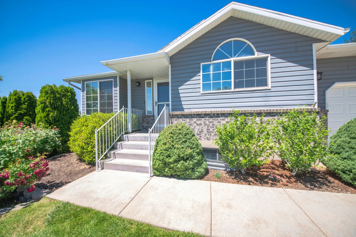Front view of a house with blue siding, surrounded by shrubs, trees, and a well-kept lawn