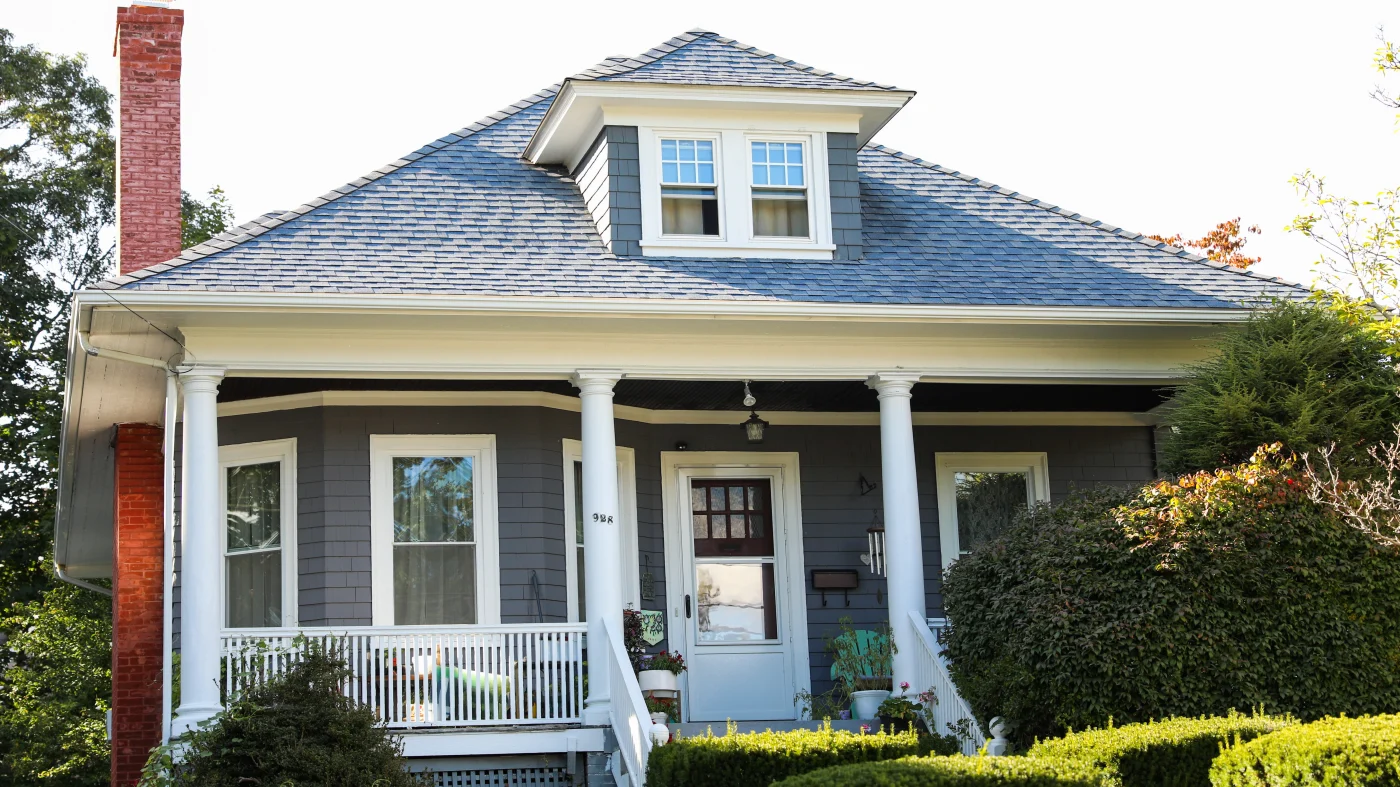 Classic home exterior with dark siding, white support beams on the front porch, and asphalt shingle roof