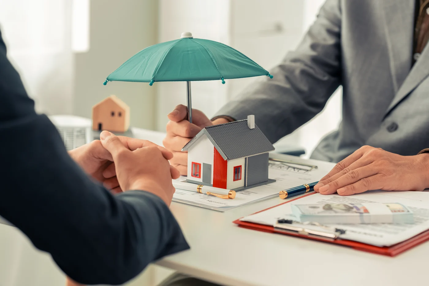 Image of people discussing home insurance over a small house with an umbrella over it