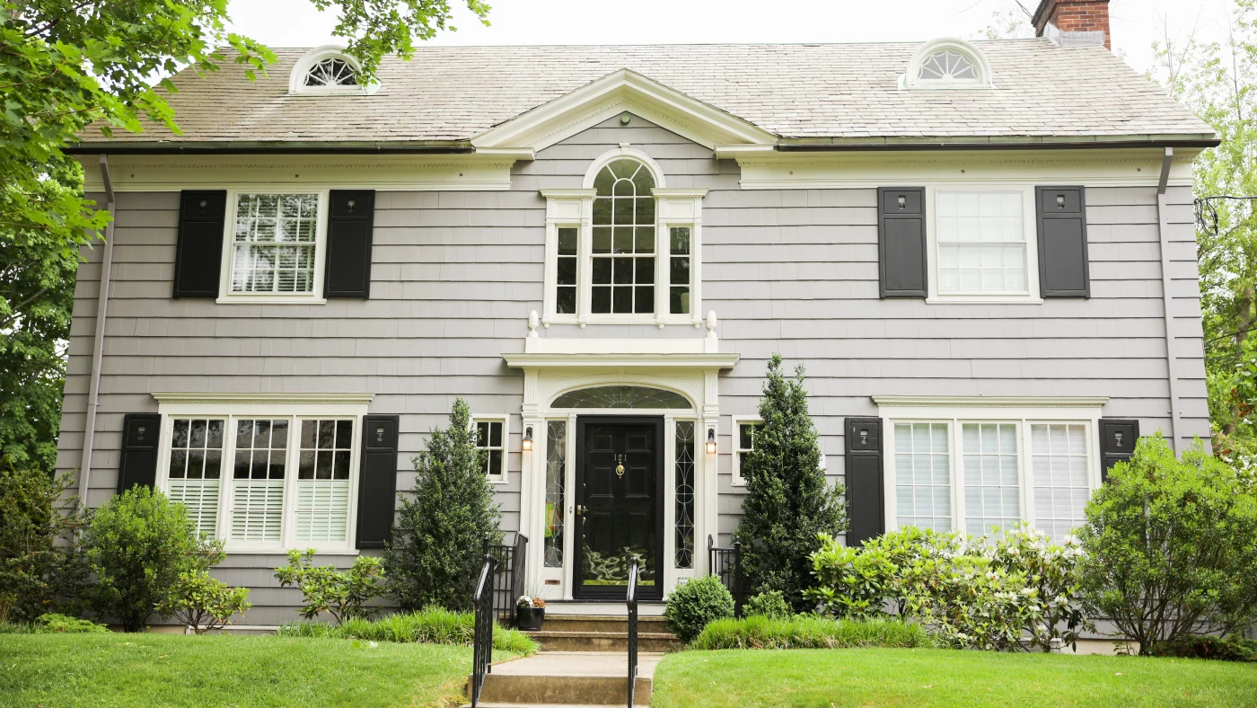Majestic two-story Suburban home with light gray siding, white framed replacement windows with black shutters, and gorgeous jet black entry door