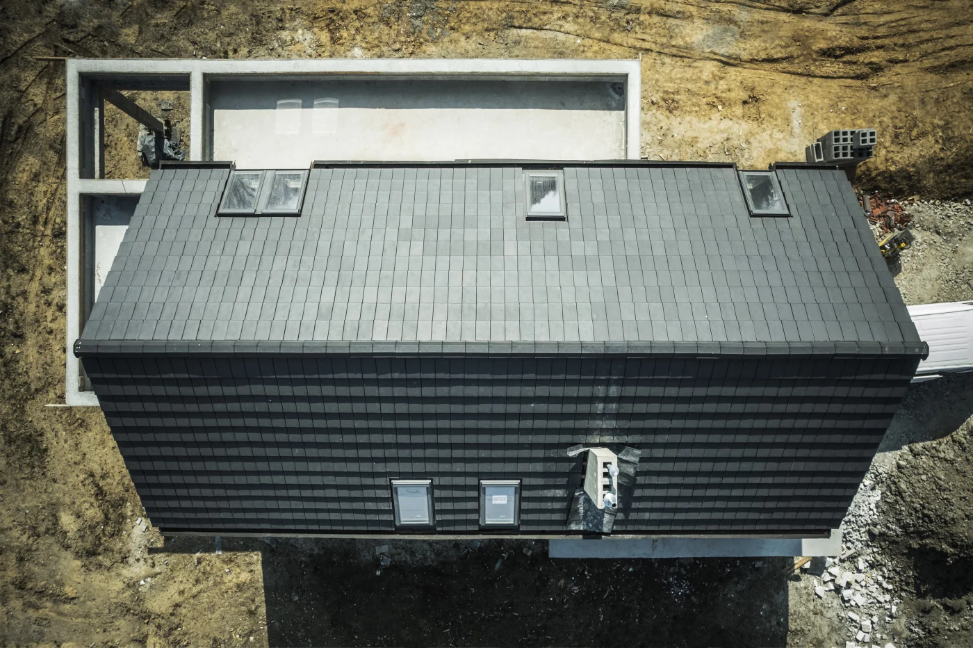 The image shows a view from above a house with a dark green, black metal roof. The house is in the country and has a small yard.