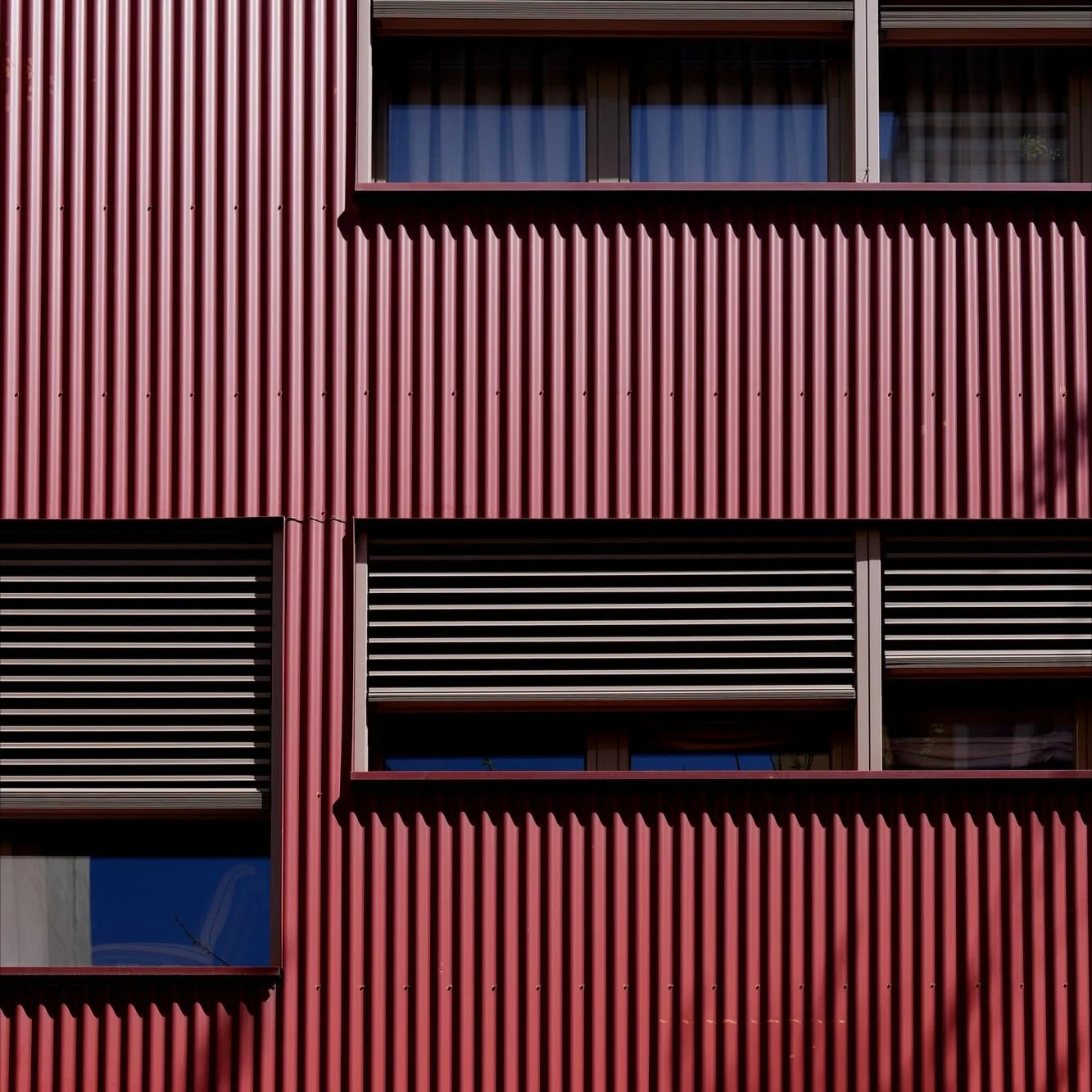 Close-up image of red aluminum metal siding on a building with many windows