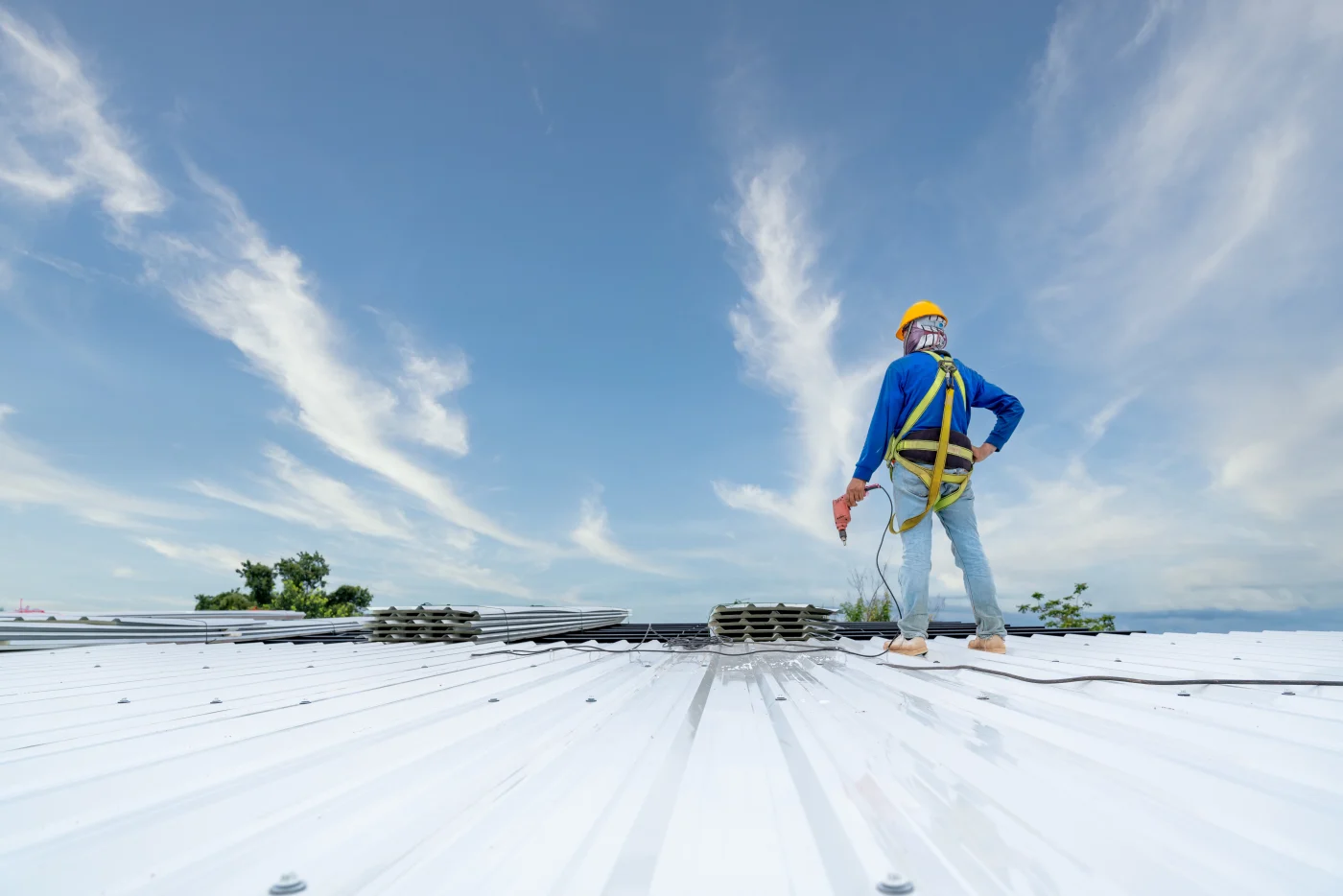 A Roofer Using Electric Drill Nail Gun Installing Pu Foam Roof Sheet At Under Construction. Safety Body Construction, Working At Height Equipment. Building A Roofer Using Electric Drill Nail Gun Installing Pu Foam Roof Sheet At Under Construction. Safety Body Construction, Working At Height Equipment. Building