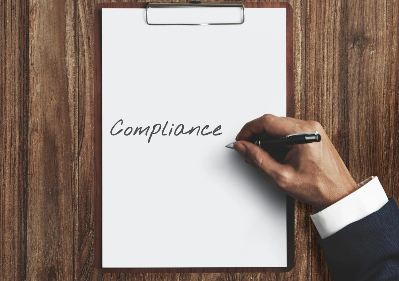 A professional hand signs a paper on a clipboard that reads, 'compliance'.