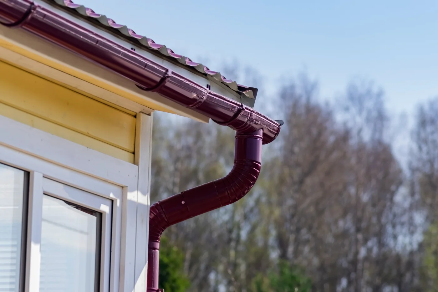 Image of bent burgundy gutters on a yellow house