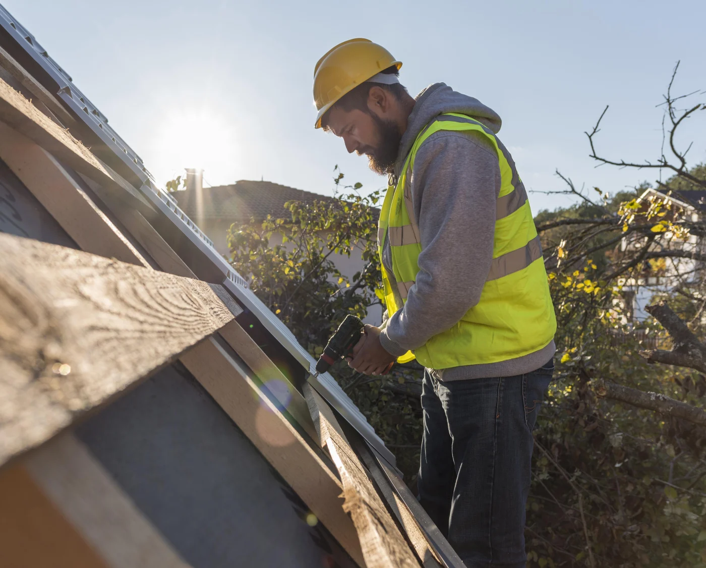 Image of a man in a yellow vest using a drill while installing a roof