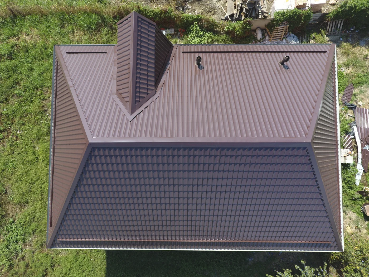The image features a small home with a brown metal roof. The yard is grassy as well.