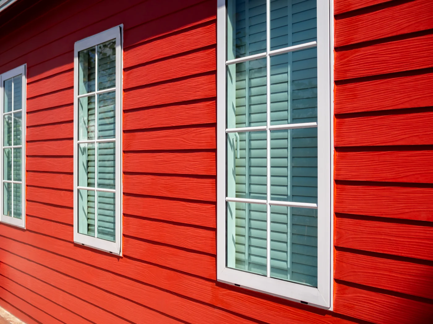 The image features a beautiful home with bold red siding. The windows are rectangular and have white frames.