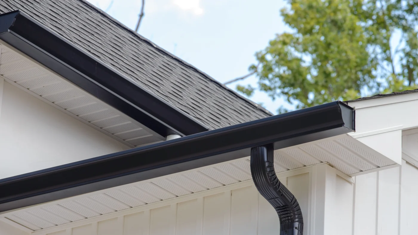 Close-up view of black gutter system and white fascia on home with white siding