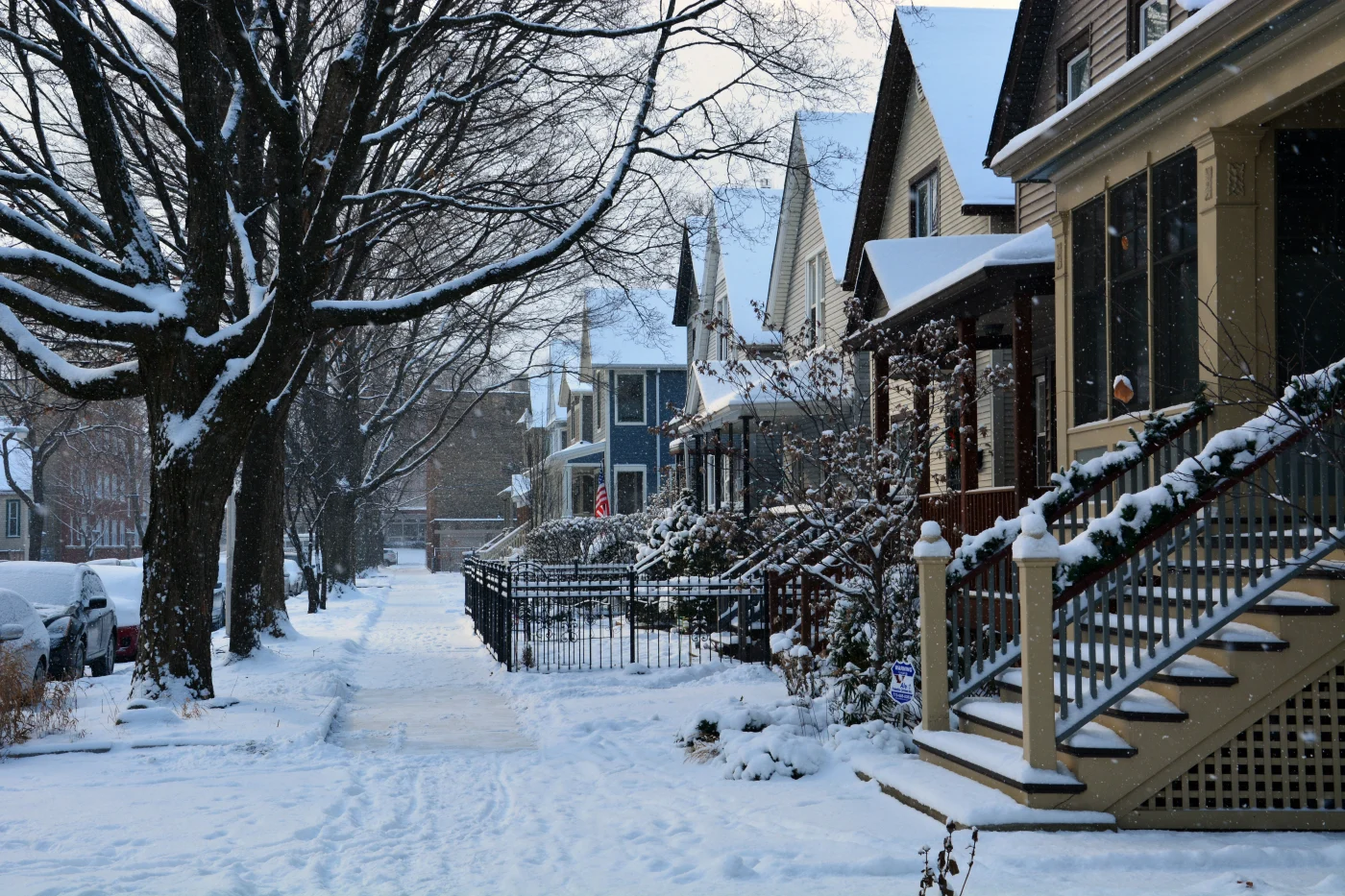 Severe Chicagoland Weather Is A Common Cause Of Roof Damage A row of homes in a Chicagoland suburb with a couple of inches of snow on the roofs, staircases, sidewalk, trees, and cars parked in the street.