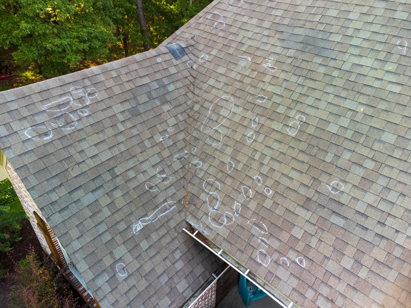 Shingle Damage And Flashing Damage Is Common In Chicagoland A drone shot of a residential asphalt shingle roof with many circular chalk marks made around hail damage after an inspection was conducted.