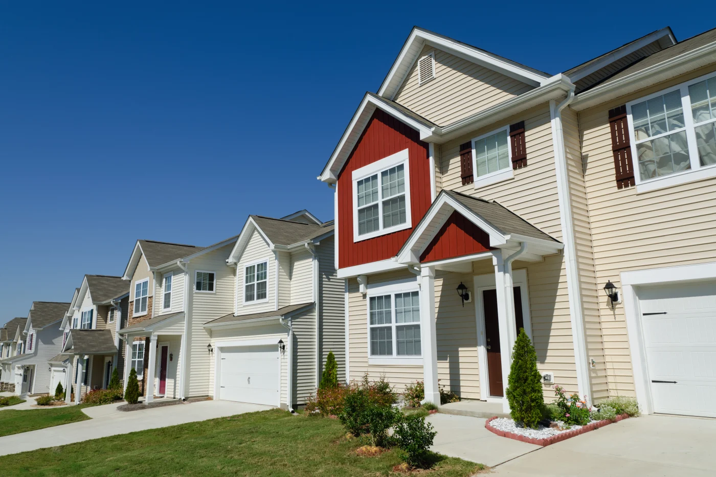 Row of townhouses with white and red vinyl siding under blue sky