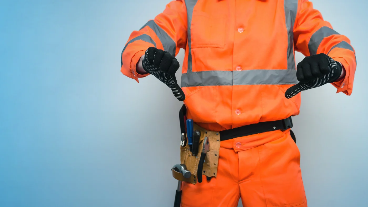 Substandard Roof Installation Causes Roof Damage Over Time A man wearing a roofer’s outfit and tool belt displaying two thumbs down, symbolizing how poor roof installation leads to roof damage, repairs, and more servicing needs.